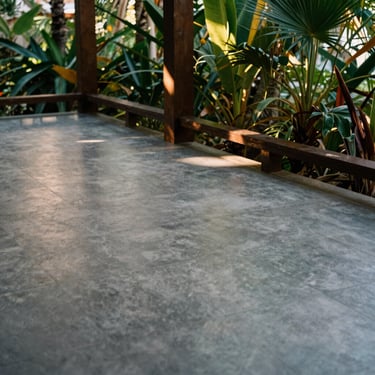 Tight detail of a hand-cast IPS floor in a shaded tropical veranda, cool grey tones, soft reflected light.