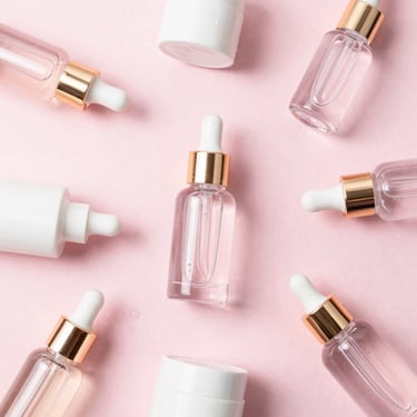 Clean flat lay of hydrating serums and creams in clear glass bottles, soft water droplets, pastel pink background, 35mm