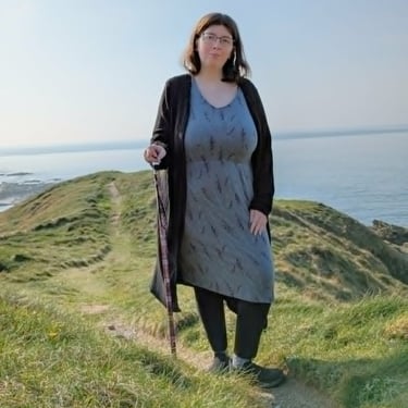 Bex standing on a coastal path with a walking stick.