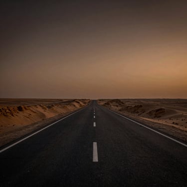 Wide environmental shot of an empty desert highway at dusk, warm bronze sky fading to deep charcoal at the edges, no figures — atmospheric, cinematic, travel-documentary