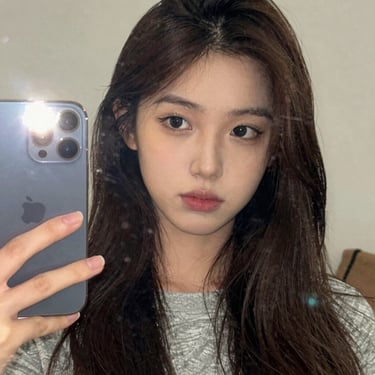 Close-up mirror selfie of a young brunette woman in casual home attire, phone flash visible, authentic social media style.