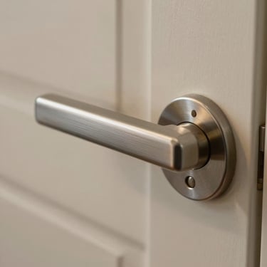 Close-up of door hardware detail, brushed metal handle and frame, clean lines, soft warm light catch on metal, minimal surrounding context