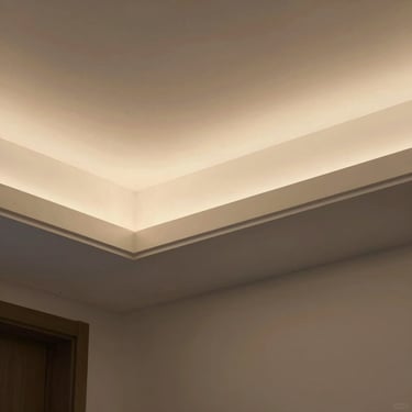 Close-up of false ceiling soffit detail with recessed linear lighting, warm ambient light pools softly, clean line where ceiling meets wall, minimal shadow