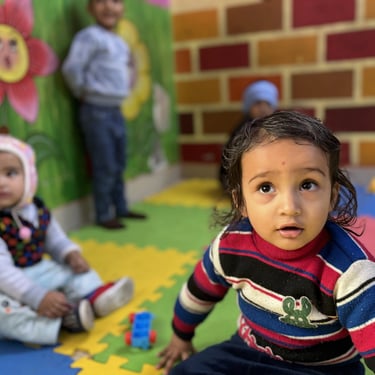 Toddlers playing in a colorful daycare center with foam mats and painted wall murals.