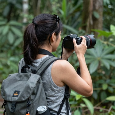 A candid portrait of a smiling traveler holding a camera against a sunset backdrop.