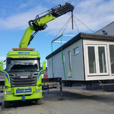 House being lifted onto a truck by a knuckle boom lorry mounted crane.