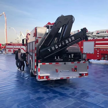 Fire truck parked on blue tarp, equipped with folding jib crane.
