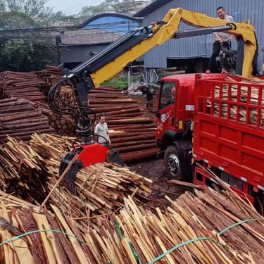 A knuckle boom truck crane loading a large pile of wood onto a truck.