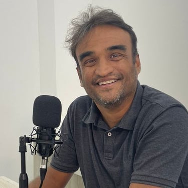 a man in a gray shirt is smiling and holding a microphone