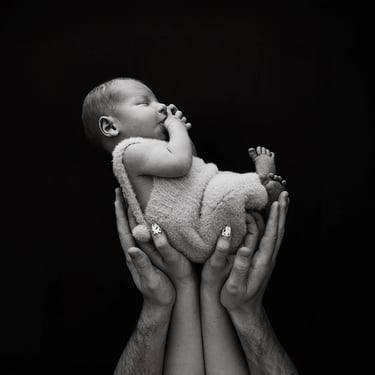 photo de bébé sur fond noir avec les main de ses parents