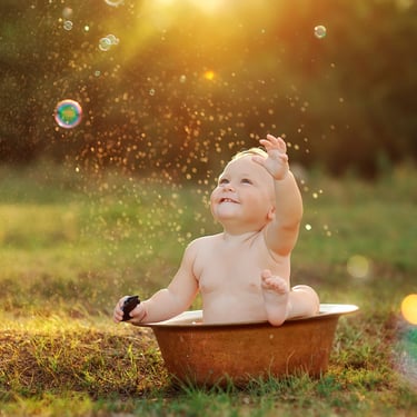 photo d’un bambin heureux dans un bassine et des bulles de savon dans un décor naturel dans les champs