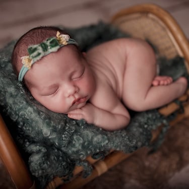 Photo de bébé endormi, délicatement posé dans un petit lit, entouré de couvertures douces et d’un petit bandeau dans les chev