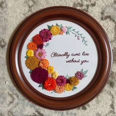 Pink, orange, and yellow 3-D embroidered flowers on white fabric in a wooden frame with the words Cliterally cunt live withou