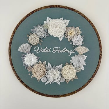 3-D embroidered flowers in whites and gray surround the words "Valid Feelings" on blue-gray fabric