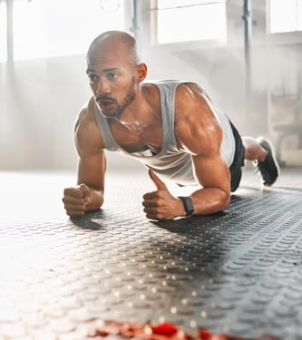 Athletic man performing a forearm plank exercise on a gym mat during a high-intensity workout.
