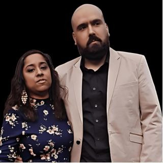 A well-dressed couple posing together, a man in a beige blazer and a woman in a floral dress.