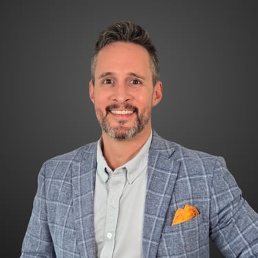Justin Hillier in a blue plaid blazer and orange pocket square smiling for a headshot.
