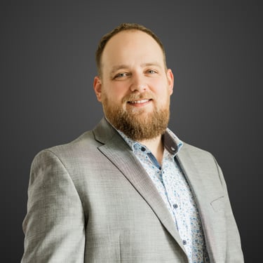 Professional headshot of a smiling Matthew Ettinger, with a beard wearing a grey blazer.