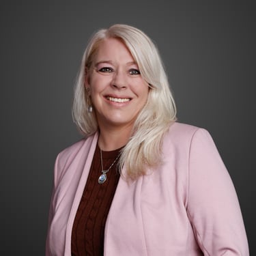Portrait of Jackie Cruickshank, a smiling blonde woman wearing a pink blazer and brown sweater.