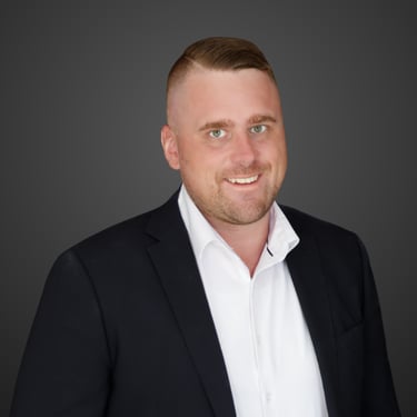 Professional headshot Riley Chisholm, a smiling man in a black suit jacket and white shirt.