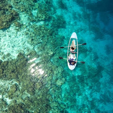 Couple kayaking in crystal-clear turquoise waters over coral reefs in the Maldives – perfect tropical adventure