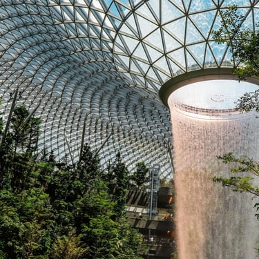 Indoor waterfall under a glass dome with lush greenery.