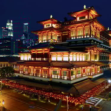 Buddha Tooth Relic Temple in Singapore Chinatown illuminated at night with modern city skyline in the background