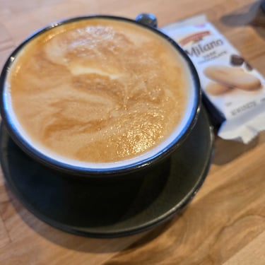 Close-up of a creamy latte in a black cup on a wooden coffee shop table