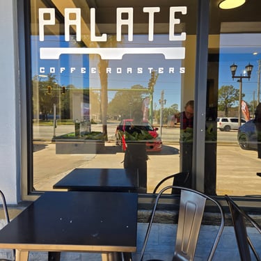 Exterior window sign of a local coffee shop with outdoor seating and patio table on a sunny day