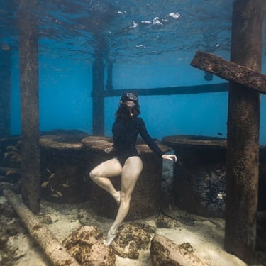 A woman posing for the camera under water surrounded by wooden pillars and ship debris.  