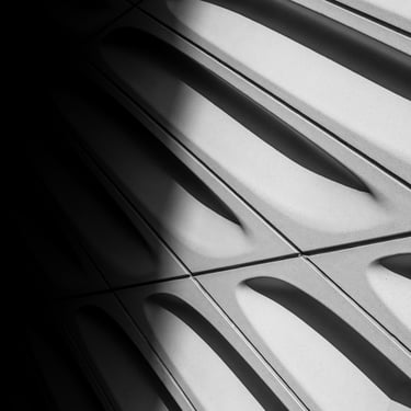 B&W image of the side of a building with a thick dark shadow covering near half of the image. The image is slanted left.