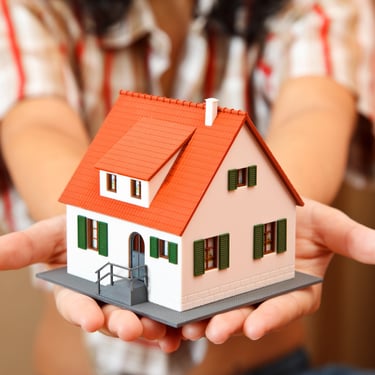 a woman holding a small model of a house