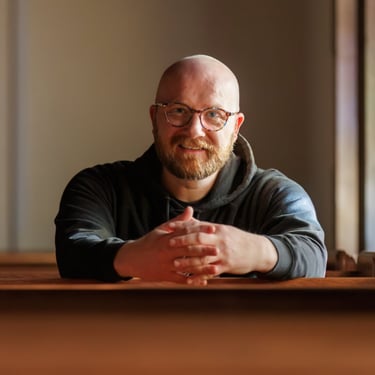 A man with glasses sitting in a church pew, smiling at the camera