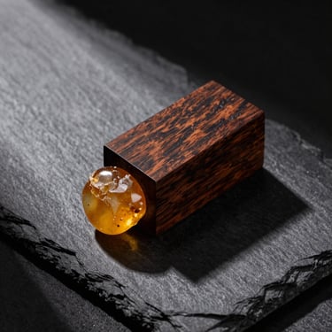 Sandalwood block and raw amber resin on dark slate, sharp directional shadows, premium editorial look