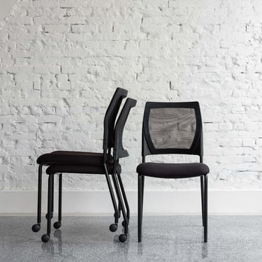 Stacked and upright V137 chairs against a white brick wall, front and side view
