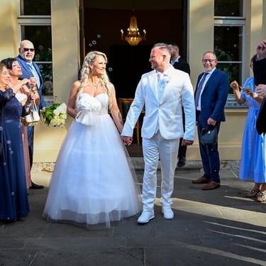 Braut und Bräutigam verlassen das Gebäude nach der Trauung, umgeben von Hochzeitsgästen mit Seifenblasen.