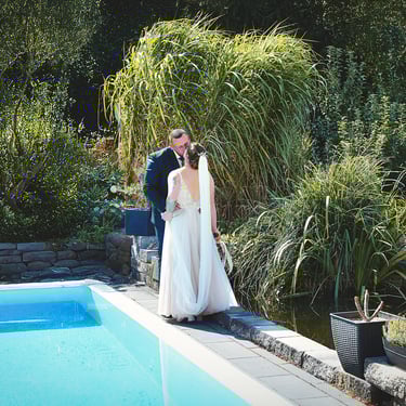 Brautpaar steht eng beieinander am Poolrand in einem Garten – ruhiger Moment einer Hochzeitsreportage.