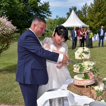 Glückliches Brautpaar beim Anschneiden der Hochzeitstorte im Freien, authentische Hochzeitsfotografie in Oranienburg.