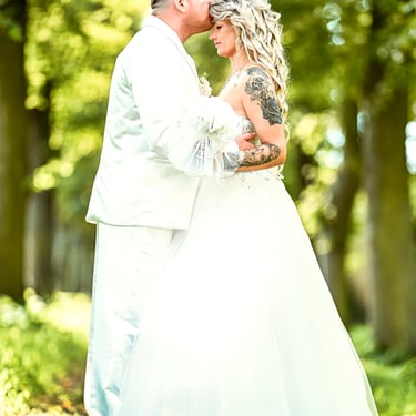 Bräutigam küsst die Stirn der Braut im Wald, emotionale Hochzeitsfotografie mit natürlichem Licht