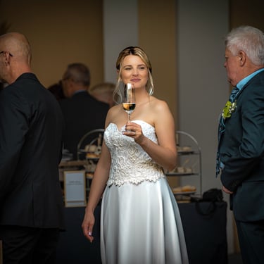 Braut beim Sektempfang hält ein Glas Sekt, Hochzeitsgäste im Hintergrund