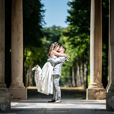 Bräutigam hebt die Braut im Säulengang, romantische Hochzeitsfotografie im Grünen