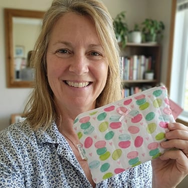 Smiling woman holding a handmade quilted makeup bag with a colorful macaron print pattern.