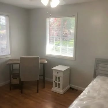 Fully furnished private bedroom for rent near Boise State including a desk, chair, nightstand, and bed with large windows.