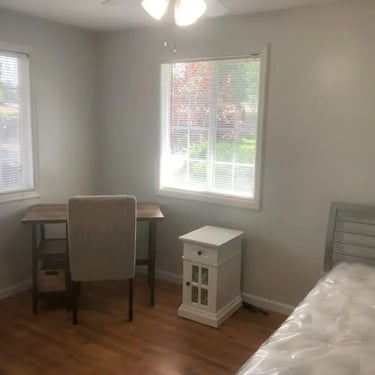 Fully furnished private bedroom for rent near Boise State including a desk, chair, nightstand, and bed with large windows.