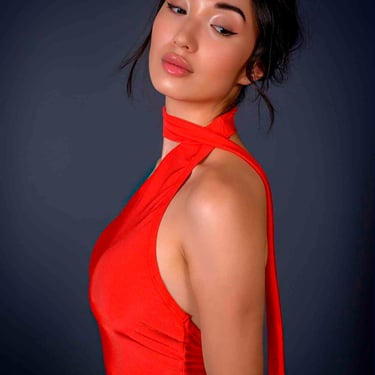 Porträt einer eleganten jungen Frau in einem leuchtend roten Kleid mit Neckholder-Ausschnitt.