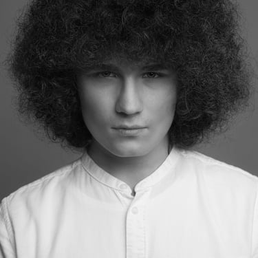 Schwarz-Weiß-Porträt eines jungen Mannes mit voluminösem Afrohaar und weißem Hemd.
