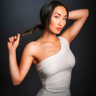 Porträt einer jungen Frau mit dunklen Haaren, die einen Zopf hält und in die Kamera blickt.