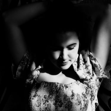 Schwarz-Weiß-Porträt einer jungen Frau in einem Blumenkleid mit den Händen über dem Kopf.