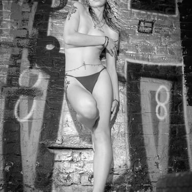 Schwarz-Weiß-Portrait einer jungen Frau mit Tattoos, oben ohne vor einer Graffiti-Wand, künstlerisch und urban inszeniert – k