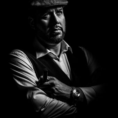 Schwarz-Weiß-Porträt eines Mannes mit Schiebermütze und Weste, der eine Zigarre hält und nachdenklich blickt.